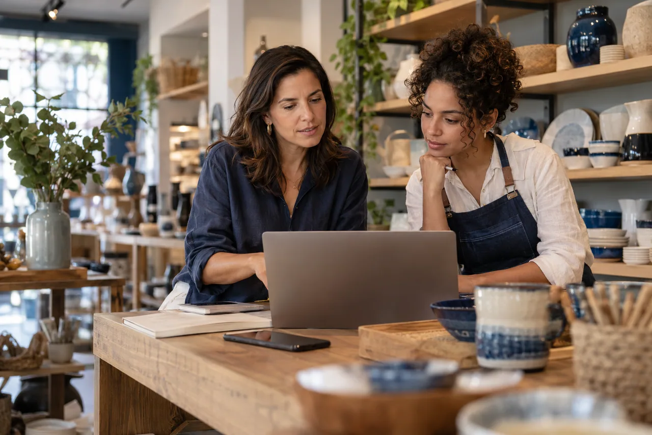 Empreendedora e colega avaliando um notebook no balcão de uma loja de utilidades.